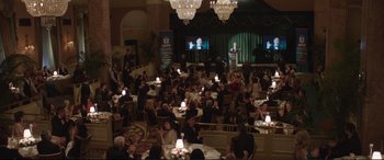 Movie still from “Miss Sloane” (2016), directed by John Madden – A crowd of people sitting at tables in front of a microphone; Extreme Wide shot, High angle