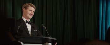Movie still from “Miss Sloane” (2016), directed by John Madden – A man standing at a podium with a microphone; Medium shot, Over the shoulder angle