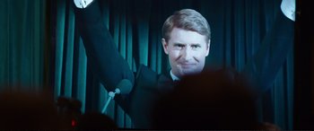 Movie still from “Miss Sloane” (2016), directed by John Madden – A man in a suit and bow tie holding a microphone; Close Up shot, Over the shoulder angle