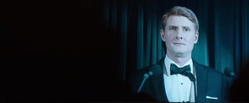Movie still from “Miss Sloane” (2016), directed by John Madden – A man in a tuxedo is speaking at a microphone; Close Up shot, Over the shoulder angle