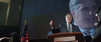 Movie still from “Miss Sloane” (2016), directed by John Madden – A man giving a speech at a podium; Medium shot, Low angle