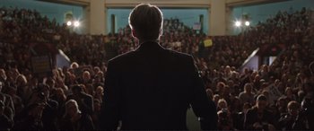 Movie still from “Miss Sloane” (2016), directed by John Madden – A man in a black suit standing in front of an audience; Medium shot, Low angle