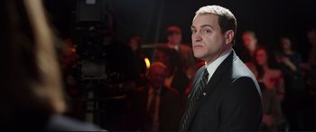 Movie still from “Miss Sloane” (2016), directed by John Madden – A man wearing a suit and tie in front of a group of people; Medium shot, Over the shoulder angle