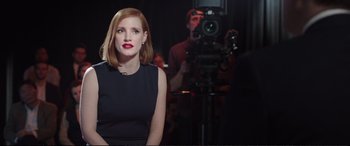 Movie still from “Miss Sloane” (2016), directed by John Madden – A woman in a black dress is in front of a video camera; Medium shot, Over the shoulder angle