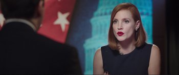 Movie still from “Miss Sloane” (2016), directed by John Madden – A woman with red lipstick sitting in front of an american flag; Close Up shot, Over the shoulder angle