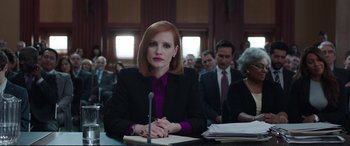 Movie still from “Miss Sloane” (2016), directed by John Madden – A woman sitting at a table in front of other people; Medium shot, Low angle