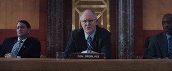 Movie still from “Miss Sloane” (2016), directed by John Madden – A man sitting at a table in front of a glass of water; Medium shot, Low angle