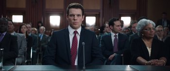 Movie still from “Miss Sloane” (2016), directed by John Madden – A man wearing a suit and tie in front of a microphone; Medium shot, Over the shoulder angle