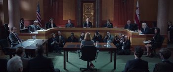 Movie still from “Miss Sloane” (2016), directed by John Madden – A woman sitting at a table in front of a group of people; Wide shot, High angle