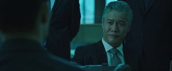 Movie still from “Night in Paradise” (2020), directed by Park Hoon-jung – A man in a suit and tie sitting in front of a table; Close Up shot, Low angle