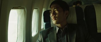 Movie still from “Night in Paradise” (2020), directed by Park Hoon-jung – A man in a suit and tie sitting on a plane; Close Up shot, Low angle