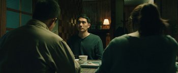 Movie still from “Night in Paradise” (2020), directed by Park Hoon-jung – A man sitting at a table with a cup in front of him; Medium shot, Over the shoulder angle