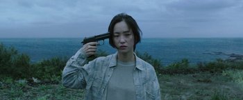 Movie still from “Night in Paradise” (2020), directed by Park Hoon-jung – A woman holding a gun up to her head; Medium shot, High angle