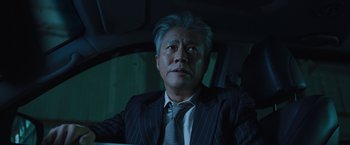 Movie still from “Night in Paradise” (2020), directed by Park Hoon-jung – An older man in a suit and tie sitting in a car; Close Up shot, Low angle