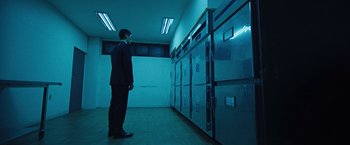 Movie still from “Night in Paradise” (2020), directed by Park Hoon-jung – A man in a suit standing in front of a wall of refrigerators; Wide shot, Low angle