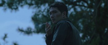 Movie still from “Night in Paradise” (2020), directed by Park Hoon-jung – A young man smoking a cigarette in the dark; Close Up shot, Low angle