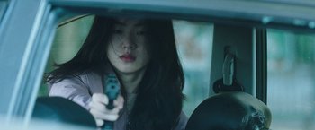 Movie still from “Night in Paradise” (2020), directed by Park Hoon-jung – A young woman holding a gun while sitting in a car; Close Up shot, Over the shoulder angle