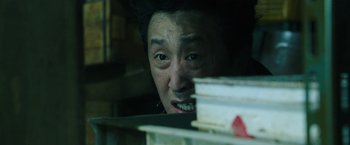 Movie still from “Night in Paradise” (2020), directed by Park Hoon-jung – A man looking at a stack of books in a dark room; Close Up shot, Low angle