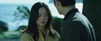 Movie still from “Night in Paradise” (2020), directed by Park Hoon-jung – A young man and a young woman standing next to each other; Close Up shot, Over the shoulder angle