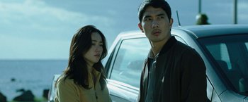 Movie still from “Night in Paradise” (2020), directed by Park Hoon-jung – A man and a woman standing in front of a white car; Medium shot, Low angle