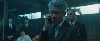 Movie still from “Night in Paradise” (2020), directed by Park Hoon-jung – A man in a suit and tie talking on a cell phone; Close Up shot, Low angle