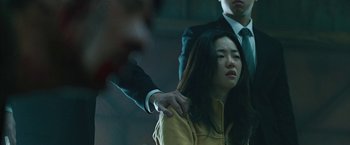 Movie still from “Night in Paradise” (2020), directed by Park Hoon-jung – A woman being held by a man in a yellow jacket; Close Up shot, Over the shoulder angle