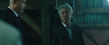 Movie still from “Night in Paradise” (2020), directed by Park Hoon-jung – A man in a suit and tie standing next to a wooden wall; Close Up shot, Low angle