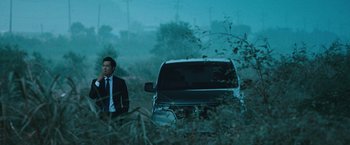 Movie still from “Night in Paradise” (2020), directed by Park Hoon-jung – A man standing in front of a car in a field; Wide shot, Low angle