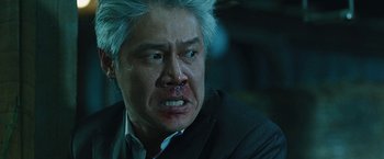 Movie still from “Night in Paradise” (2020), directed by Park Hoon-jung – An asian man with white hair and a bruised face; Close Up shot, Low angle