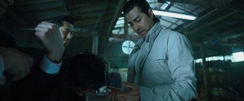 Movie still from “Night in Paradise” (2020), directed by Park Hoon-jung – A man in a white shirt is looking at his cell phone; Medium shot, Over the shoulder angle