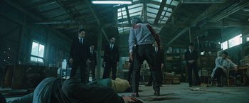 Movie still from “Night in Paradise” (2020), directed by Park Hoon-jung – A group of men standing around in a warehouse; Wide shot, Low angle