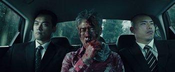 Movie still from “Night in Paradise” (2020), directed by Park Hoon-jung – A man with blood all over his face sitting in the back seat of a car; Medium shot, Over the shoulder angle