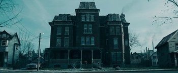 Movie still from “No One Gets Out Alive” (2021), directed by Santiago Menghini – An old house with many windows on a cloudy day; Extreme Wide shot, Low angle
