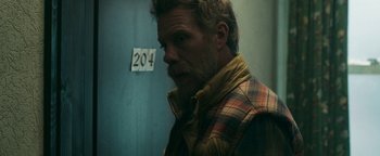 Movie still from “No One Gets Out Alive” (2021), directed by Santiago Menghini – A man in a plaid vest standing in front of a wall; Close Up shot, Over the shoulder angle