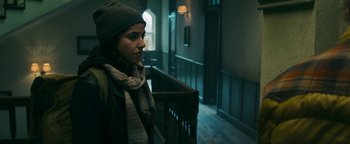 Movie still from “No One Gets Out Alive” (2021), directed by Santiago Menghini – A woman wearing a hat and scarf standing in a hallway; Close Up shot, Low angle