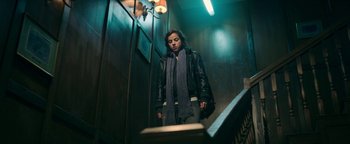 Movie still from “No One Gets Out Alive” (2021), directed by Santiago Menghini – A person wearing a black jacket and a blue scarf; Medium shot, Low angle