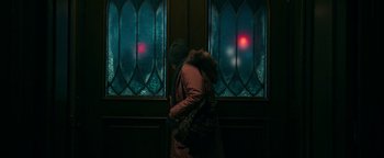 Movie still from “No One Gets Out Alive” (2021), directed by Santiago Menghini – A person standing in front of stained glass windows at night; Medium shot, Over the shoulder angle