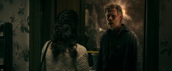 Movie still from “No One Gets Out Alive” (2021), directed by Santiago Menghini – A man and a woman are standing in front of a window; Medium shot, Over the shoulder angle