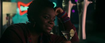 Movie still from “No One Gets Out Alive” (2021), directed by Santiago Menghini – A woman sitting at a table holding a martini glass; Close Up shot, Over the shoulder angle