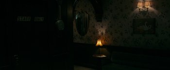 Movie still from “No One Gets Out Alive” (2021), directed by Santiago Menghini – A dimly - lit room with a lamp on a table; Wide shot, High angle