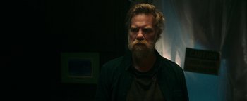 Movie still from “No One Gets Out Alive” (2021), directed by Santiago Menghini – A man with a long beard is looking into the distance; Medium shot, Low angle