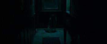 Movie still from “No One Gets Out Alive” (2021), directed by Santiago Menghini – A woman sitting on the floor in a dark room; Wide shot, High angle