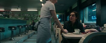 Movie still from “No One Gets Out Alive” (2021), directed by Santiago Menghini – A woman sitting at a table in front of a man; Medium shot, Over the shoulder angle