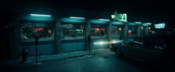 Movie still from “No One Gets Out Alive” (2021), directed by Santiago Menghini – A car parked on the side of the road next to a building; Extreme Wide shot, High angle