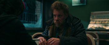 Movie still from “No One Gets Out Alive” (2021), directed by Santiago Menghini – A man with a beard and a jacket on is looking at his cell phone; Medium shot, Over the shoulder angle