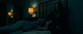 Movie still from “No One Gets Out Alive” (2021), directed by Santiago Menghini – Two women are laying in a dark room; Medium shot, High angle