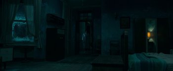 Movie still from “No One Gets Out Alive” (2021), directed by Santiago Menghini – A person standing in a dark room in front of an open door; Extreme Wide shot, High angle
