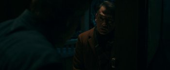 Movie still from “No One Gets Out Alive” (2021), directed by Santiago Menghini – A man standing in a dark room with his eyes closed; Medium shot, Over the shoulder angle