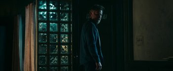 Movie still from “No One Gets Out Alive” (2021), directed by Santiago Menghini – A man with a beard standing in front of a window; Medium shot, Low angle