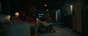 Movie still from “No One Gets Out Alive” (2021), directed by Santiago Menghini – A woman sitting on the floor of a living room next to a television; Wide shot, High angle